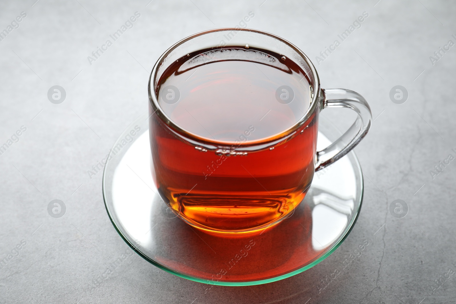 Photo of Refreshing black tea in cup on grey textured table, closeup