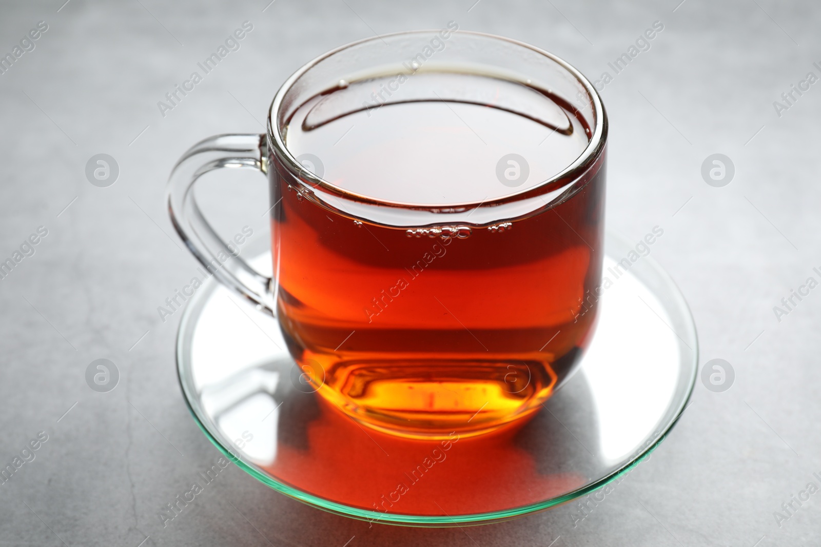 Photo of Refreshing black tea in cup on grey textured table, closeup