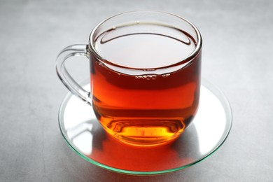 Photo of Refreshing black tea in cup on grey textured table, closeup