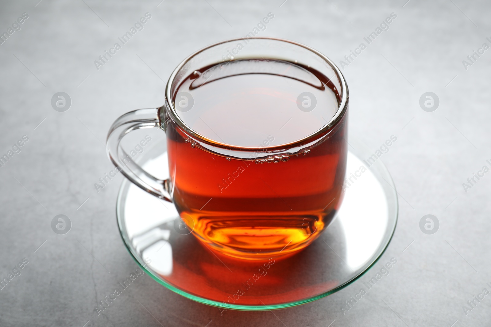 Photo of Refreshing black tea in cup on grey textured table, closeup