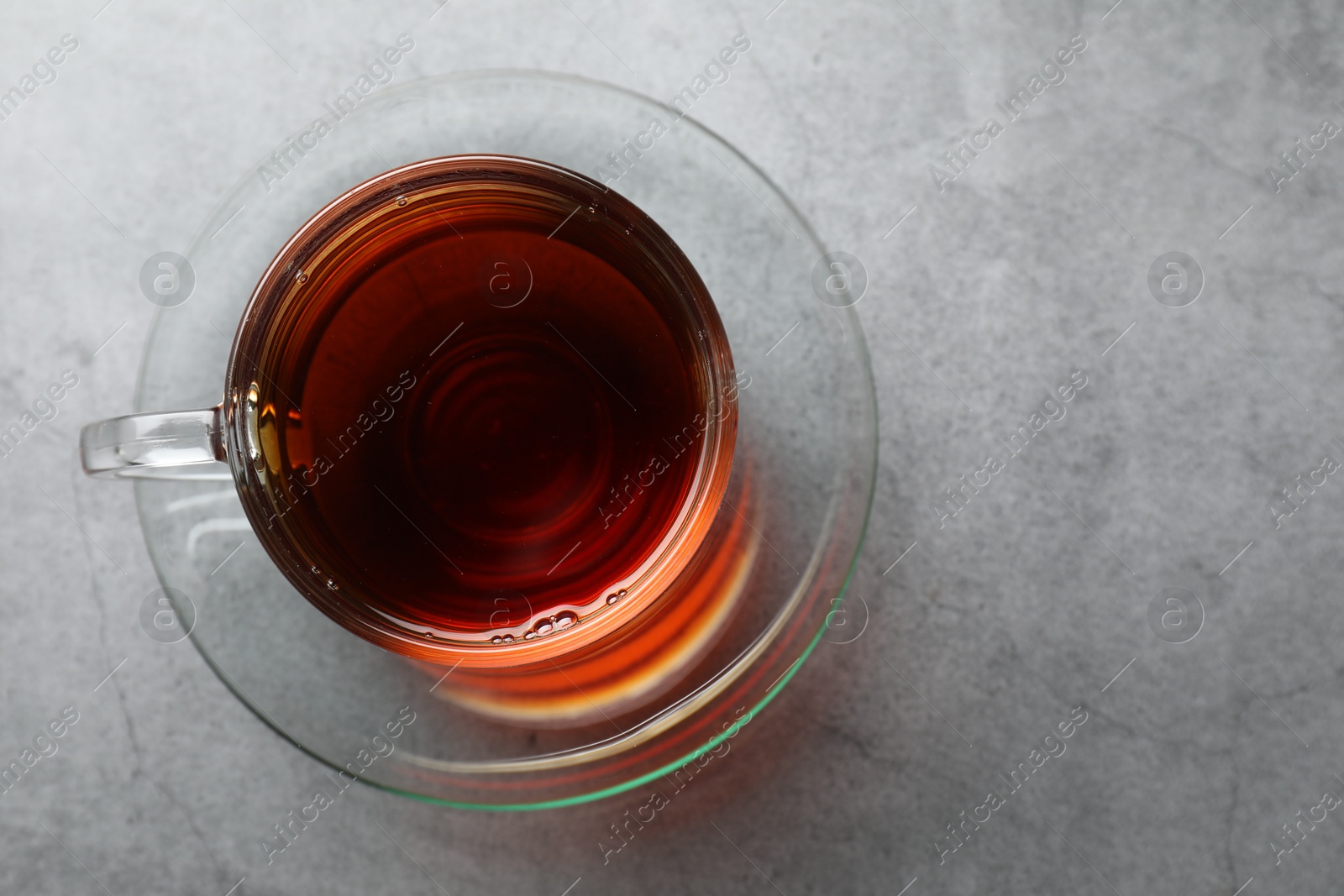 Photo of Refreshing black tea in cup on grey textured table, top view. Space for text