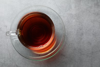 Photo of Refreshing black tea in cup on grey textured table, top view. Space for text