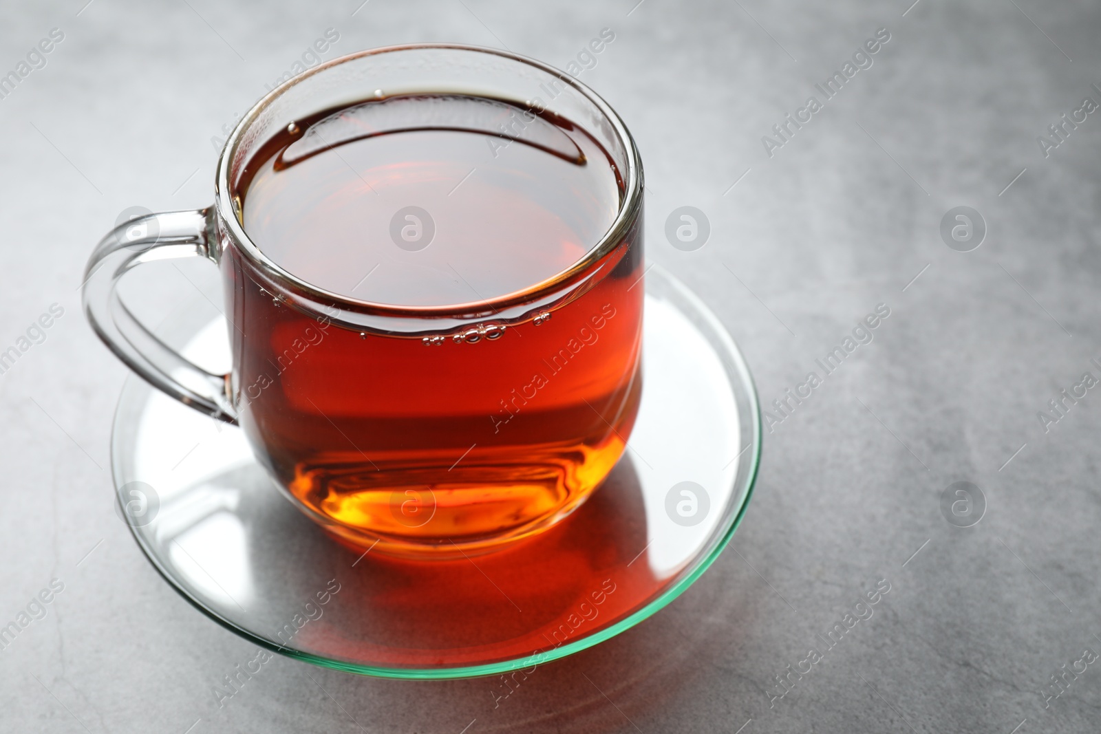 Photo of Refreshing black tea in cup on grey textured table, closeup. Space for text