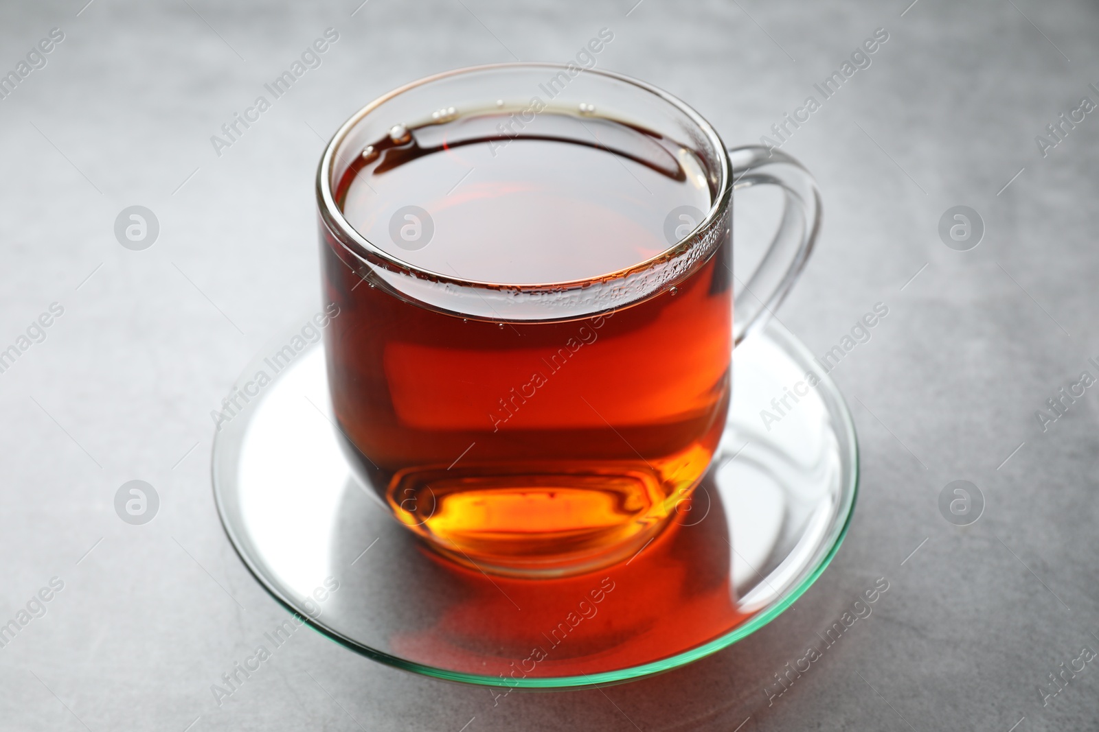 Photo of Refreshing black tea in cup on grey table, closeup