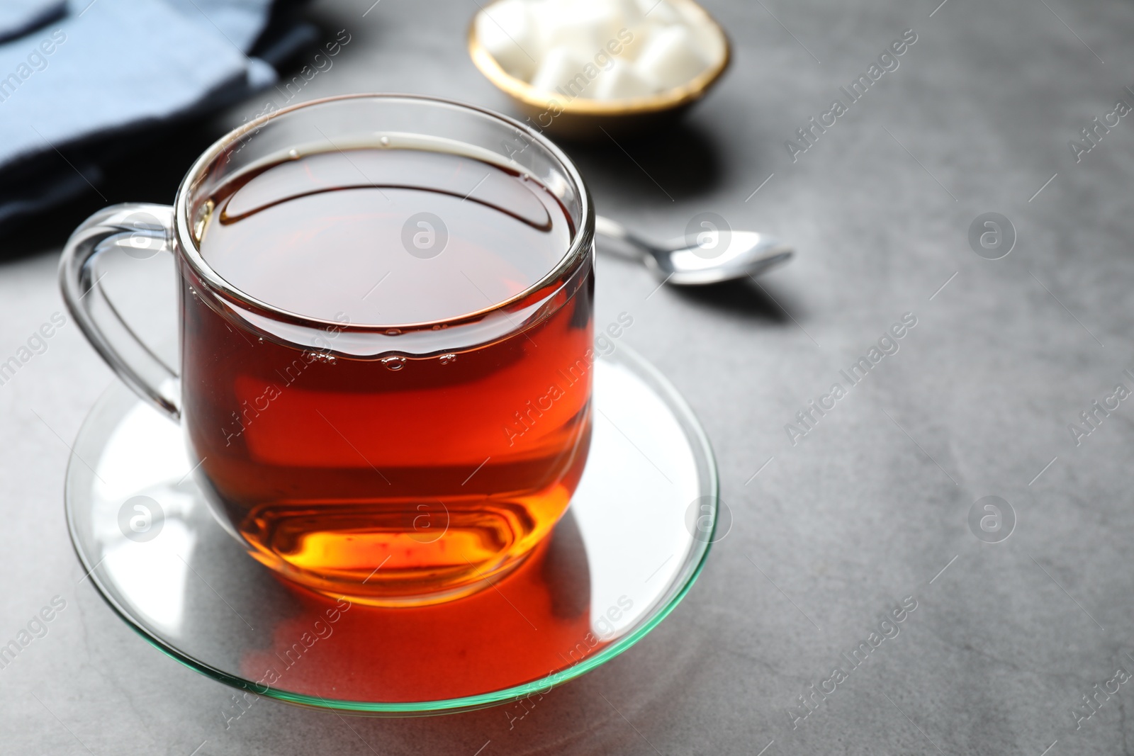 Photo of Refreshing black tea in cup on grey textured table, closeup. Space for text