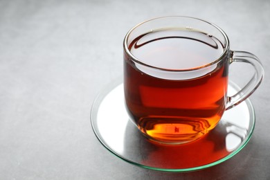 Photo of Refreshing black tea in cup on grey table, closeup. Space for text