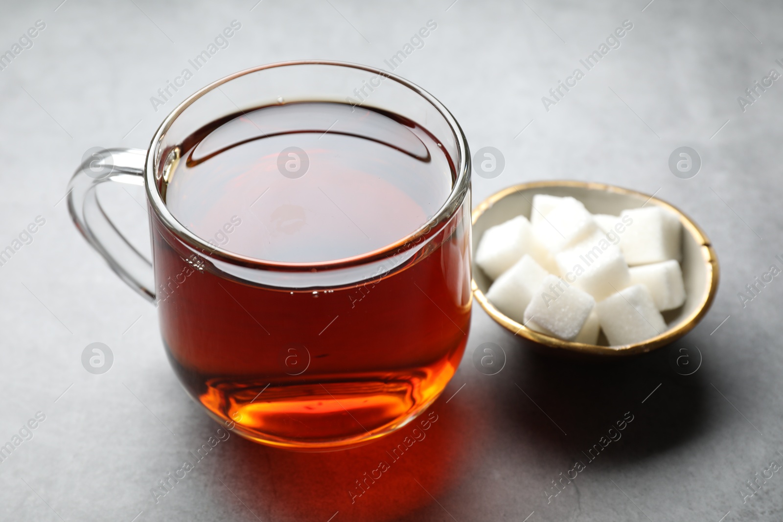 Photo of Refreshing black tea in cup and sugar cubes on grey table, closeup