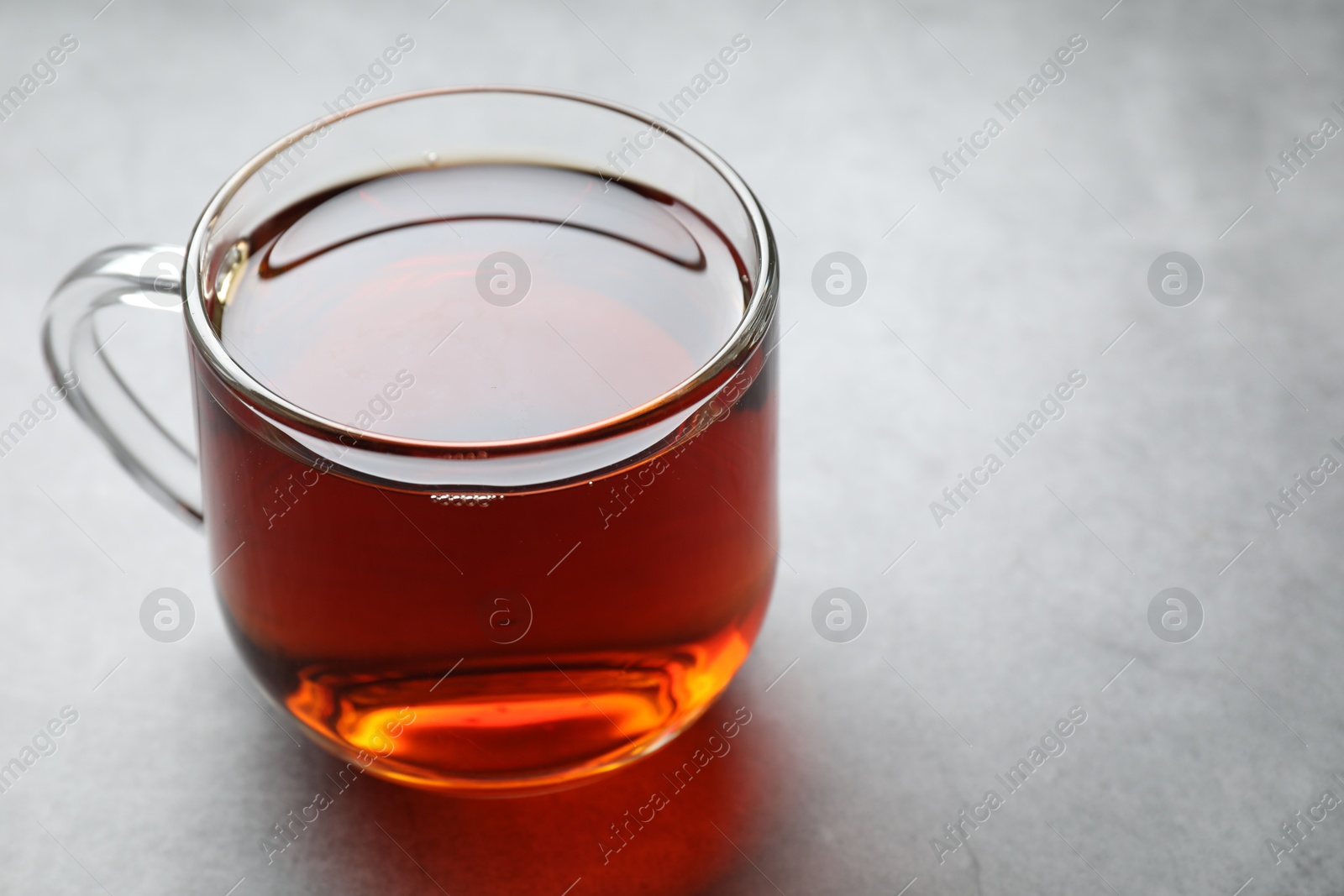 Photo of Refreshing black tea in cup on grey table, closeup. Space for text