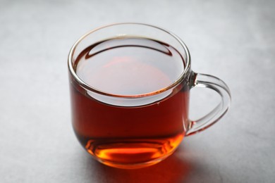 Photo of Refreshing black tea in cup on grey table, closeup