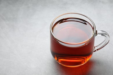 Photo of Refreshing black tea in cup on grey table, closeup. Space for text