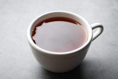 Photo of Refreshing black tea in cup on grey table, closeup