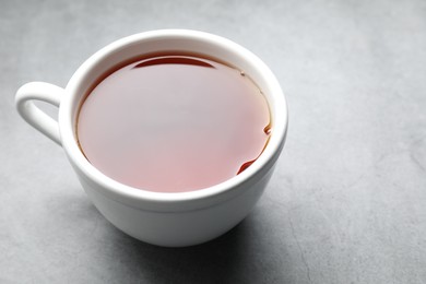 Photo of Refreshing black tea in cup on grey table, closeup