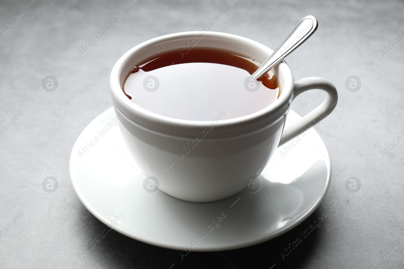 Photo of Refreshing black tea and spoon in cup on grey textured table, closeup