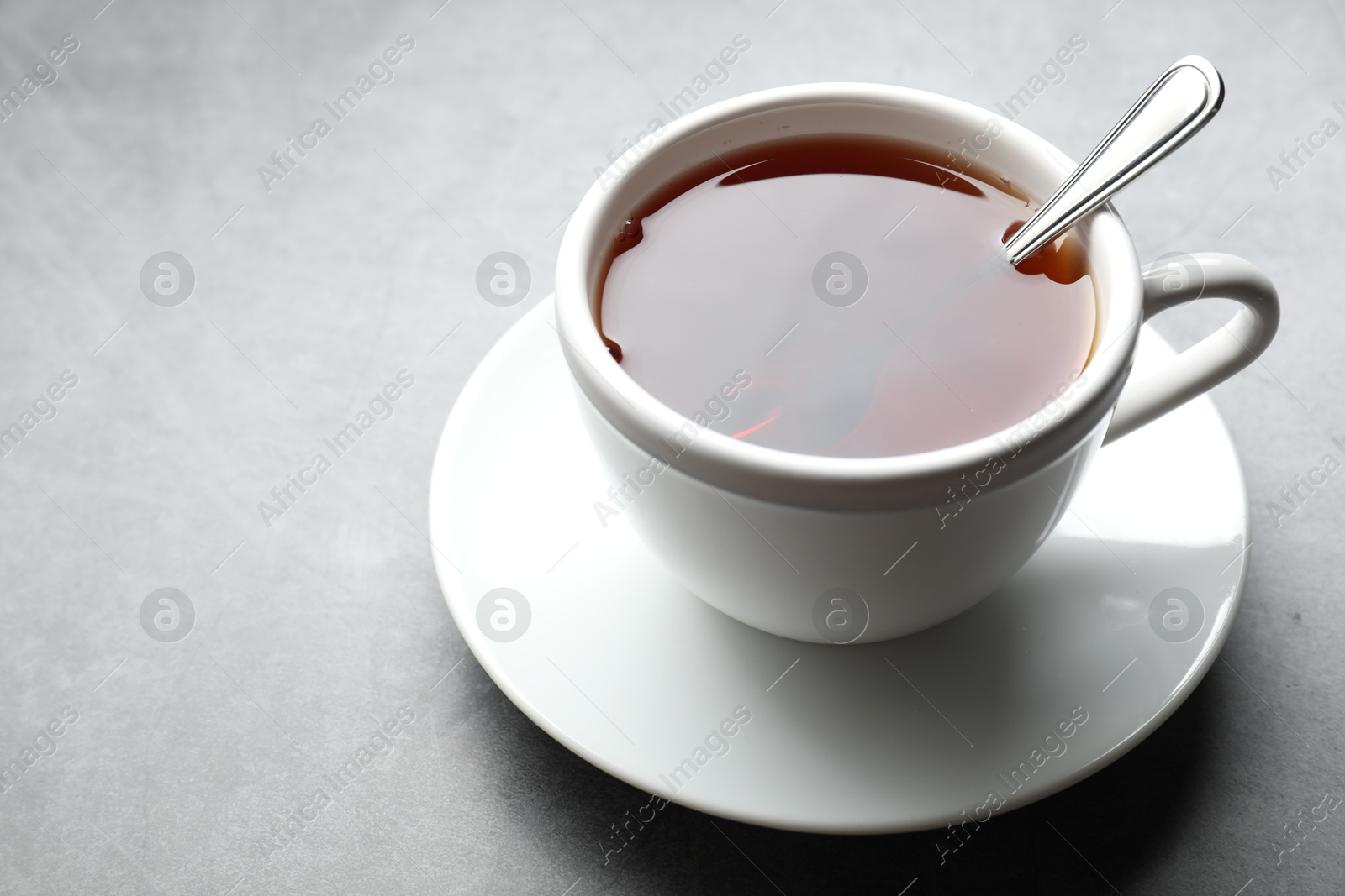 Photo of Refreshing black tea and spoon in cup on grey textured table, closeup. Space for text