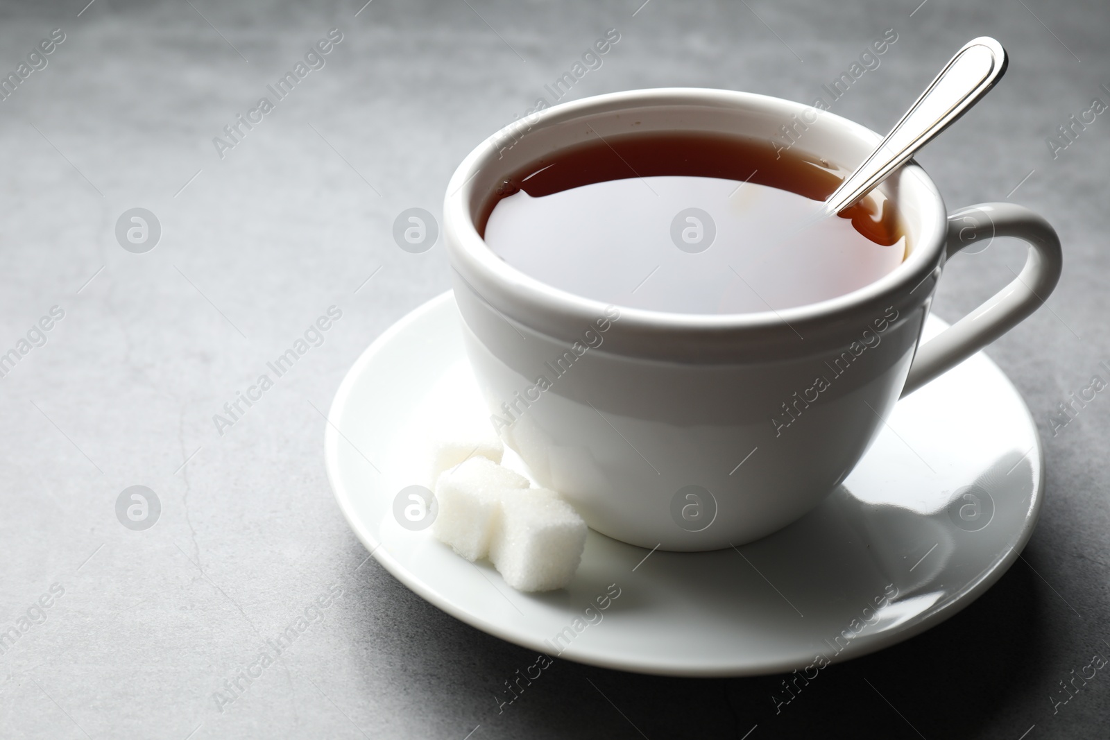 Photo of Refreshing black tea in cup and sugar cubes on grey textured table, closeup. Space for text