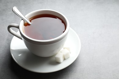 Photo of Refreshing black tea in cup and sugar cubes on grey textured table, closeup. Space for text