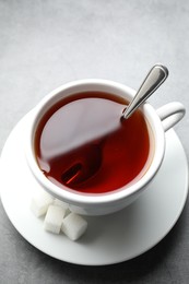 Photo of Refreshing black tea in cup and sugar cubes on grey textured table, above view