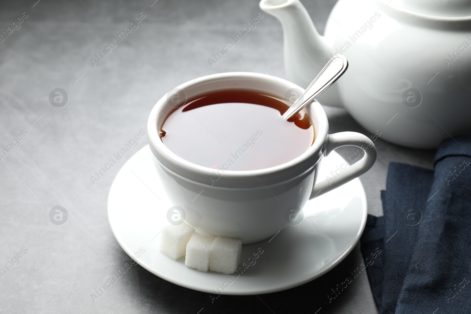 Photo of Refreshing black tea in cup and sugar cubes on grey textured table, closeup