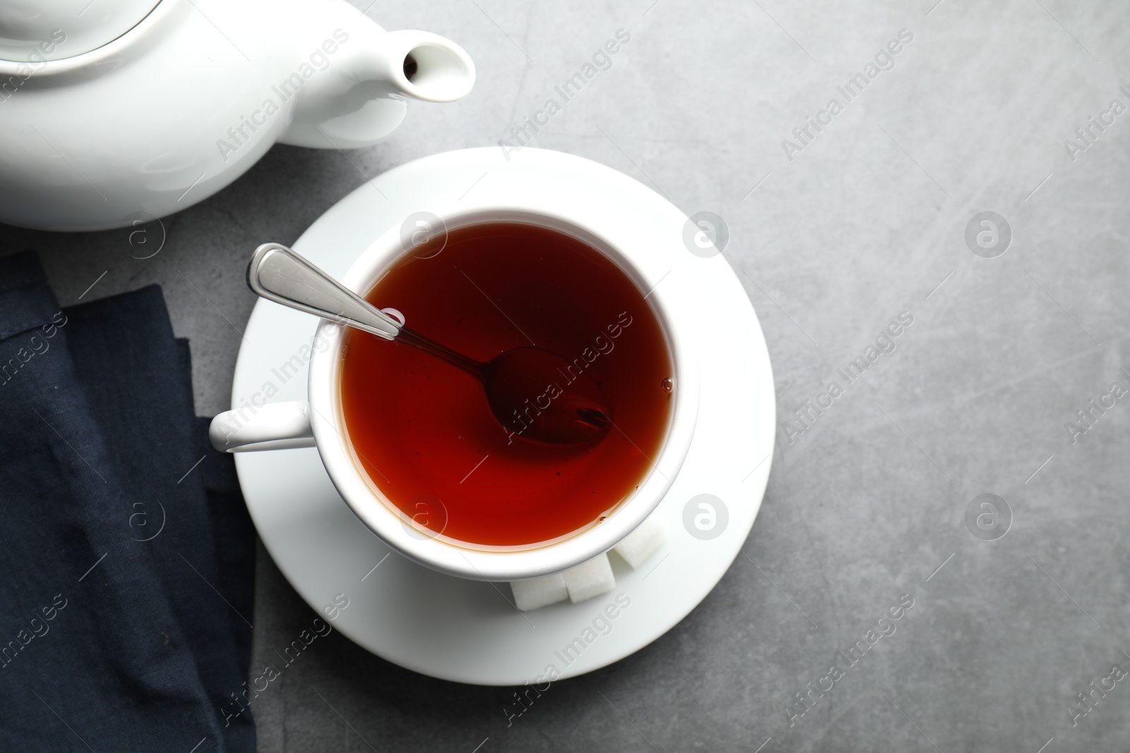 Photo of Refreshing black tea in cup, sugar cubes and teapot on grey textured table, flat lay. Space for text