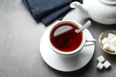 Photo of Refreshing black tea in cup, sugar cubes and teapot on grey textured table, above view. Space for text