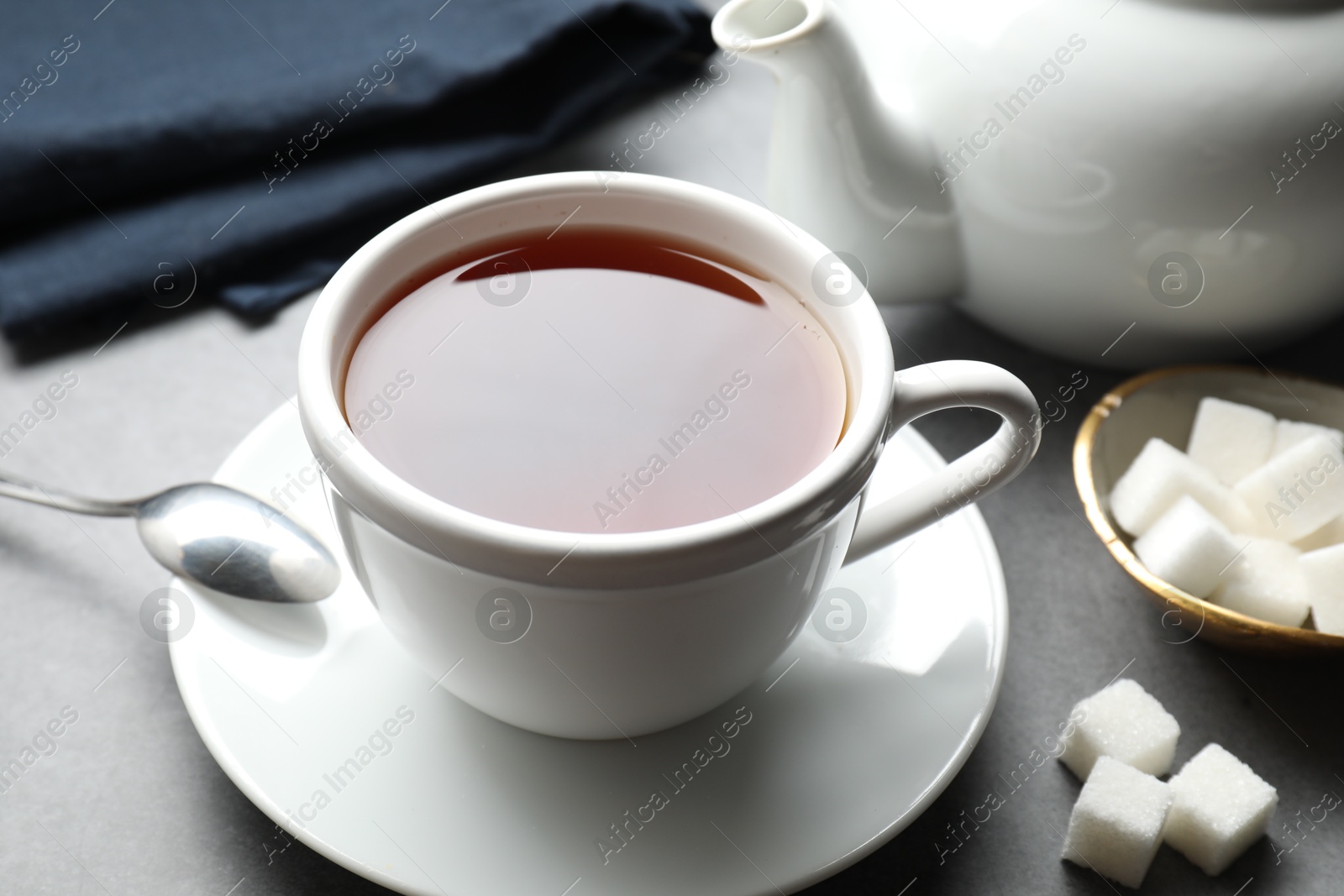 Photo of Refreshing black tea in cup and sugar cubes on grey textured table, closeup