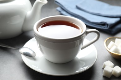 Photo of Refreshing black tea in cup and sugar cubes on grey textured table, closeup