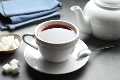 Photo of Refreshing black tea in cup and sugar cubes on grey textured table, closeup