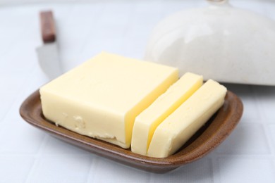 Photo of Cut tasty butter in dish on white tiled table, closeup