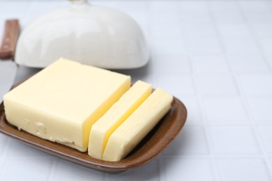 Photo of Cut tasty butter in dish on white tiled table, closeup. Space for text