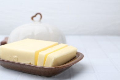 Photo of Cut tasty butter in dish on white tiled table, closeup. Space for text