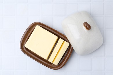 Photo of Cut tasty butter in dish on white tiled table, top view