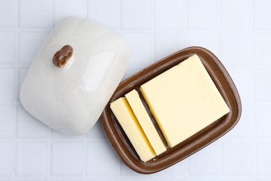 Photo of Cut tasty butter in dish on white tiled table, top view