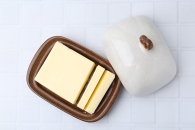 Photo of Cut tasty butter in dish on white tiled table, top view