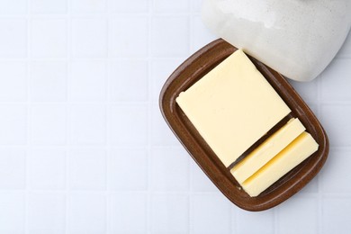 Photo of Cut tasty butter in dish on white tiled table, top view. Space for text