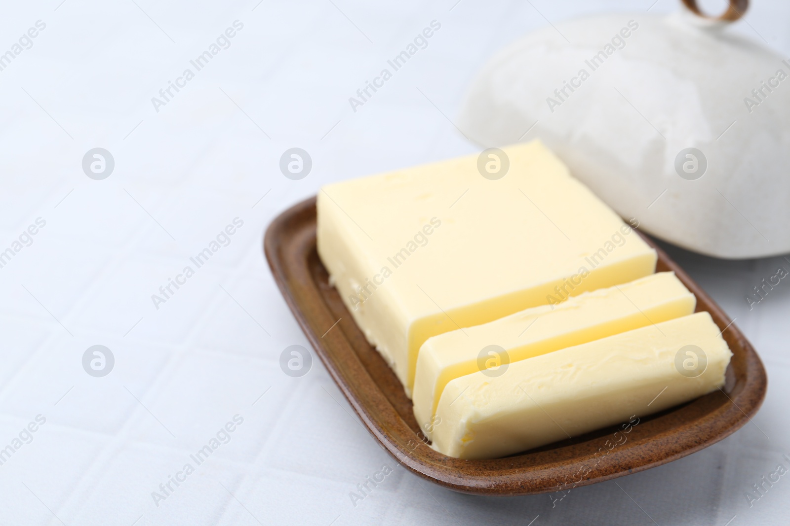 Photo of Cut tasty butter in dish on light grey table, closeup. Space for text