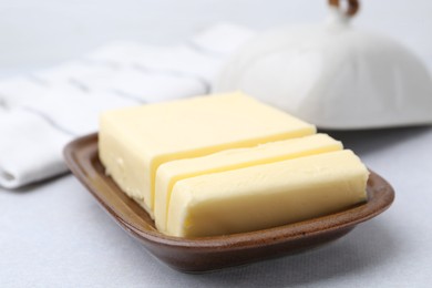 Photo of Cut tasty butter in dish on light grey table, closeup