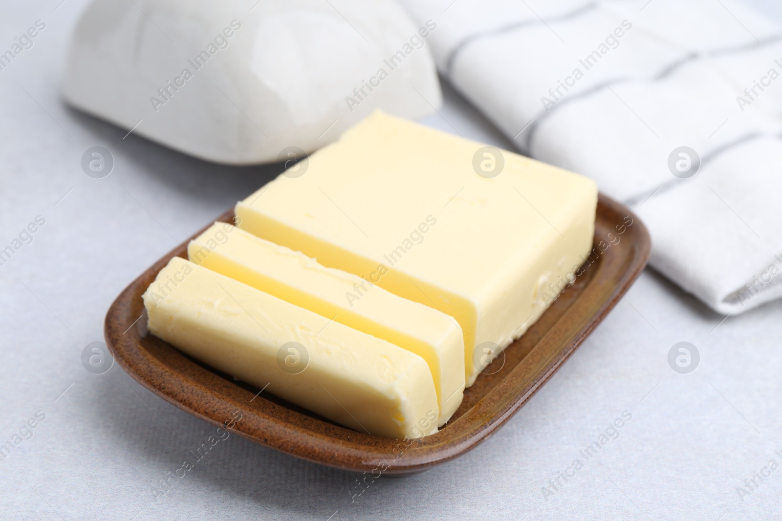 Photo of Cut tasty butter in dish on light grey table, closeup