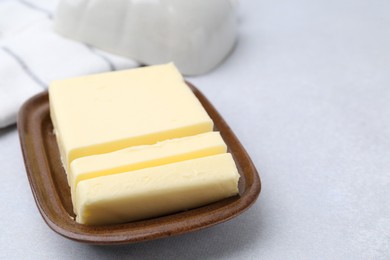 Photo of Cut tasty butter in dish on light grey table, closeup. Space for text