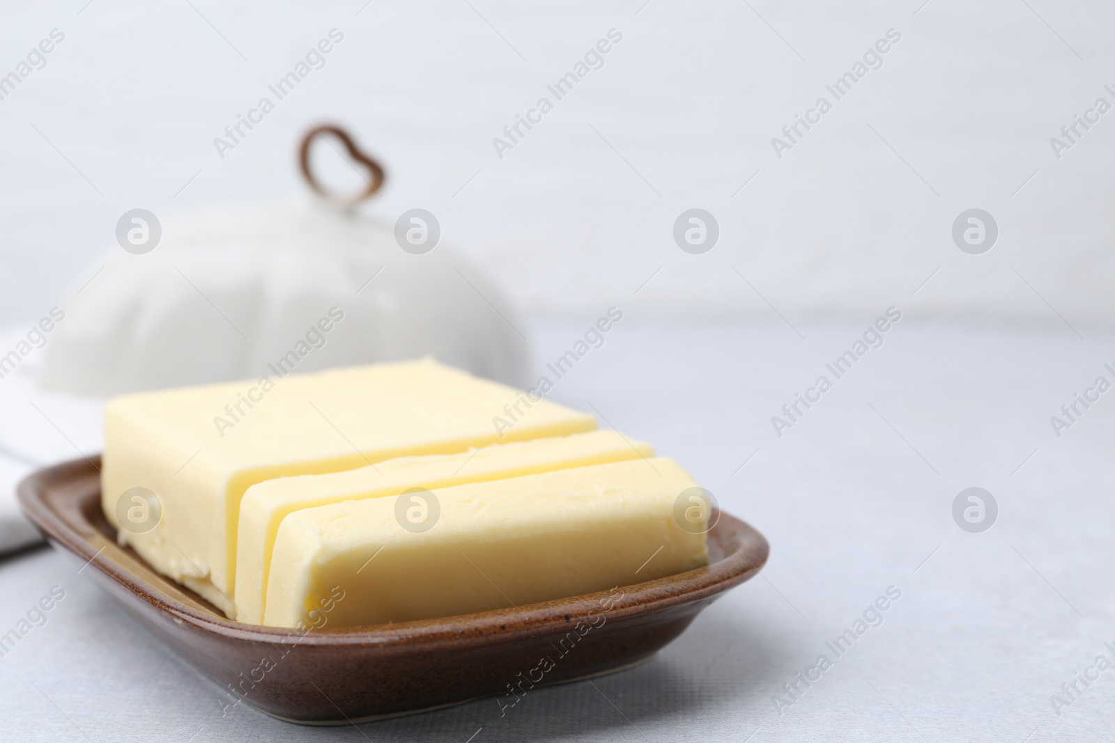 Photo of Cut tasty butter in dish on light grey table, closeup. Space for text