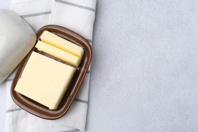 Photo of Cut tasty butter in dish on light grey table, top view. Space for text