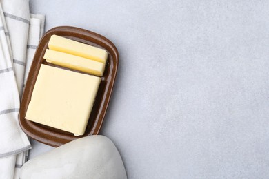 Photo of Cut tasty butter in dish on light grey table, top view. Space for text