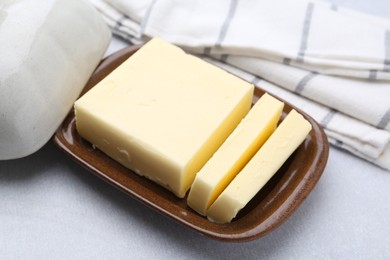 Photo of Cut tasty butter in dish on light grey table, closeup