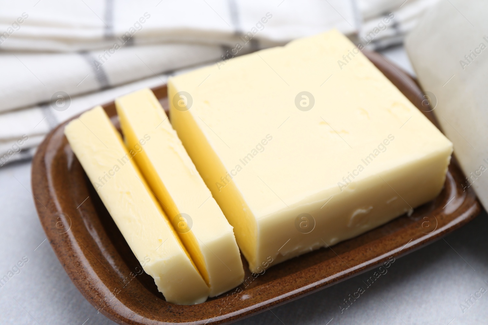 Photo of Cut tasty butter in dish on light grey table, closeup