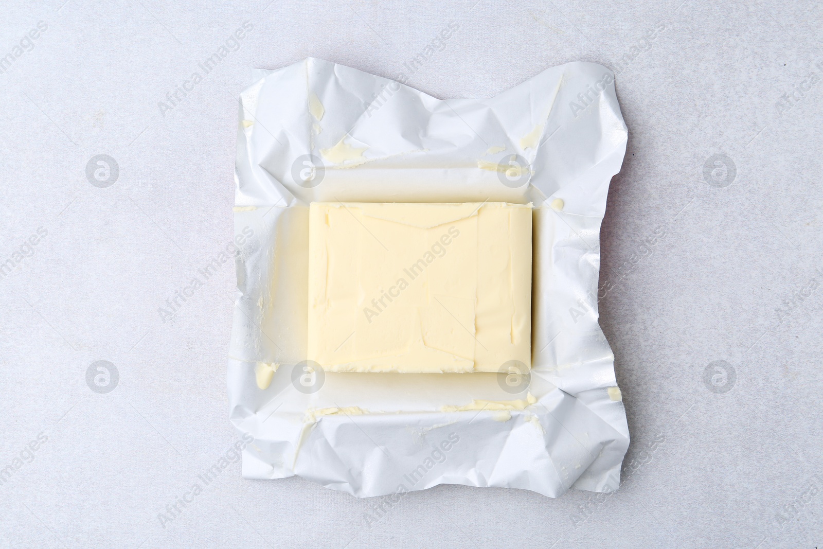 Photo of Block of tasty butter in open package on light grey table, top view