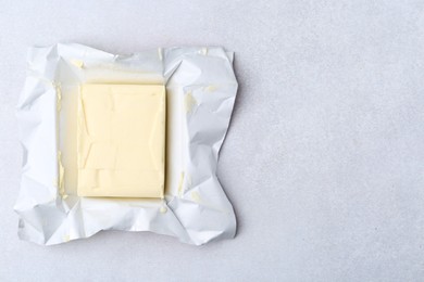 Photo of Block of tasty butter in open package on light grey table, top view. Space for text