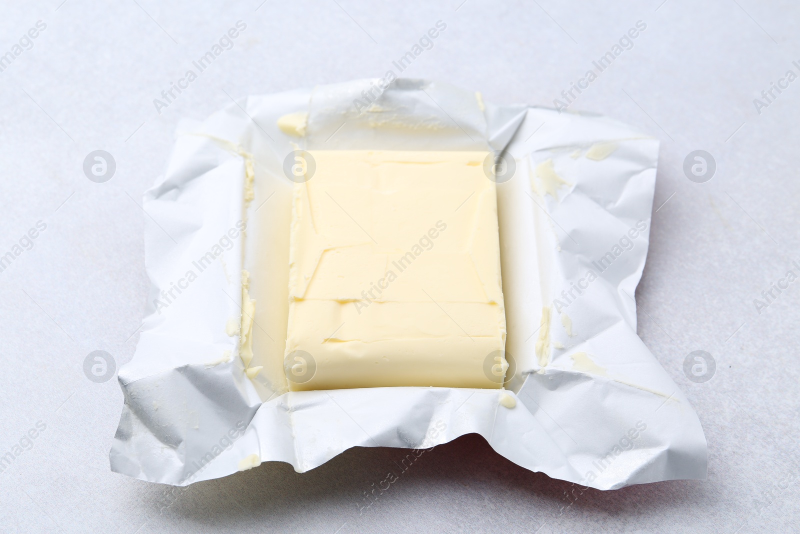 Photo of Block of tasty butter in open package on light grey table, closeup