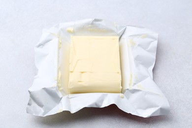 Photo of Block of tasty butter in open package on light grey table, closeup