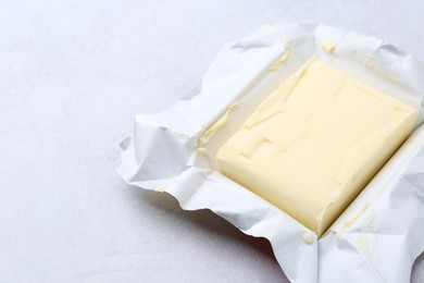 Photo of Block of tasty butter in open package on light grey table, closeup. Space for text