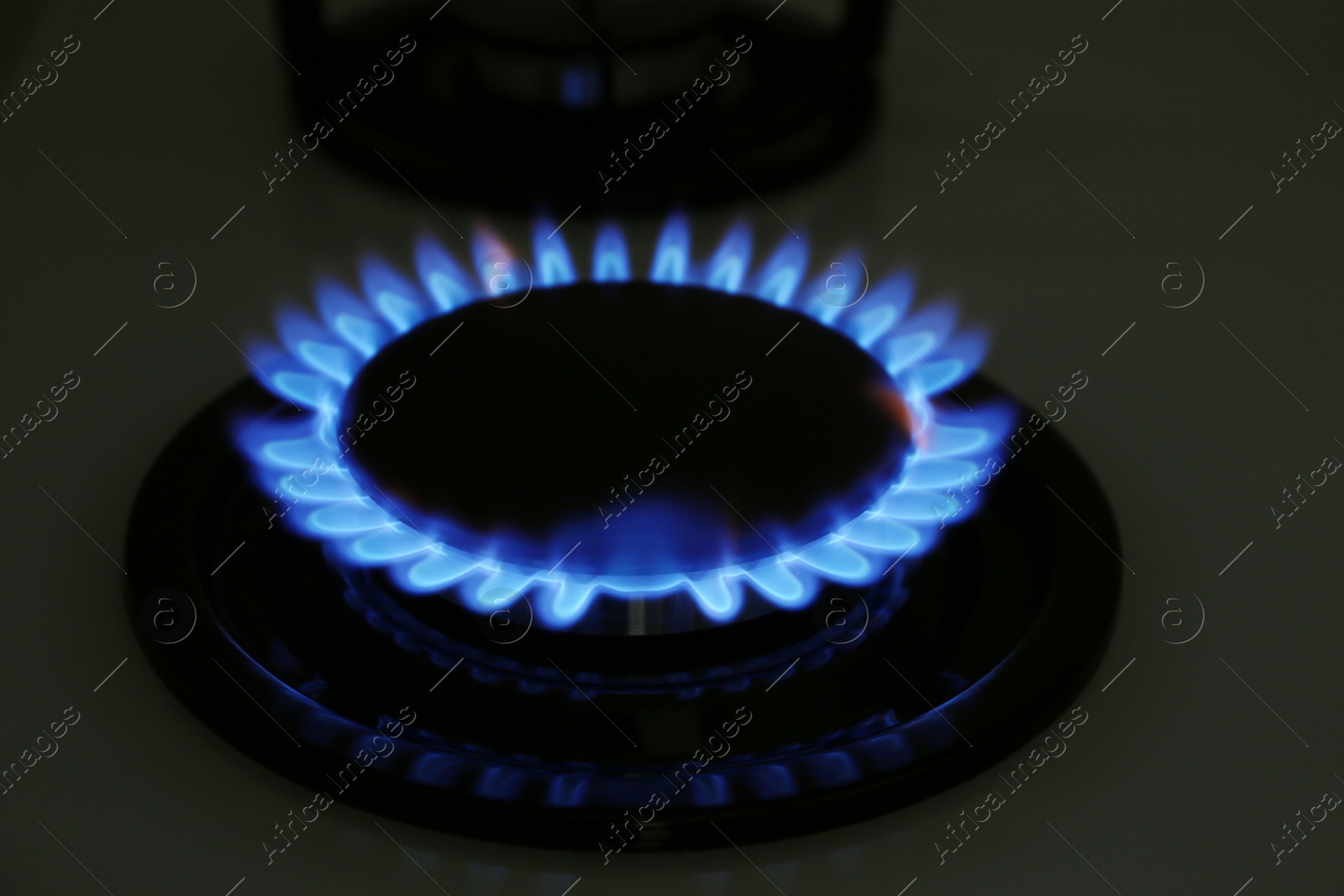 Photo of Gas burner of modern stove with burning blue flame at night, closeup