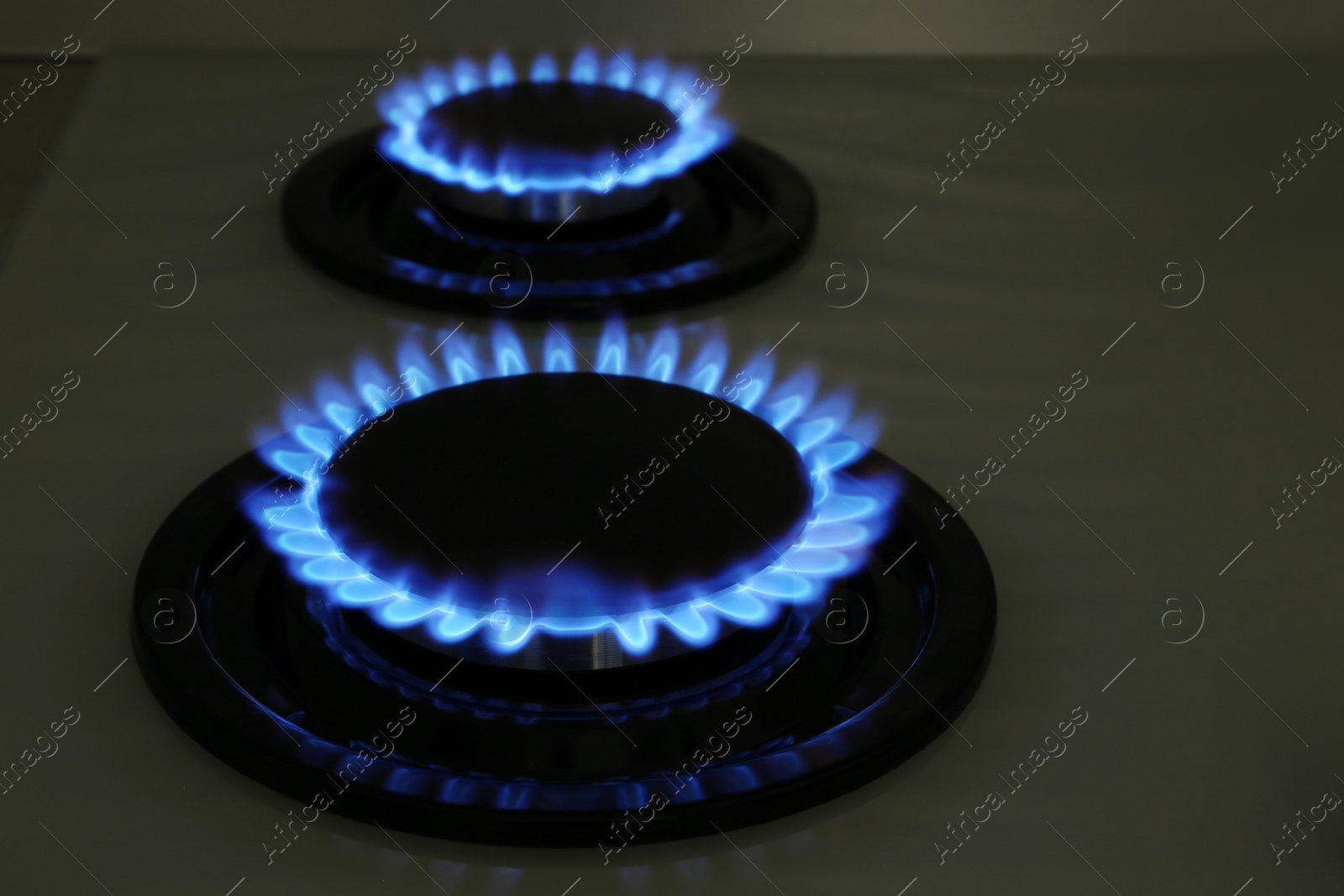 Photo of Modern gas cooktop with burning blue flames in kitchen at night